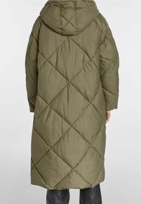 Olivgrön puffjacka med huva, med ett diamantmönstrat quiltat mönster och lång längd. Tillverkad av ett slätt, lätt material.