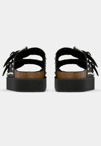 Sandales à plateforme en caoutchouc noir avec un design découpé, des clous argentés le long des brides, et une semelle intermédiaire en liège. Semelle extérieure texturée pour une meilleure adhérence.