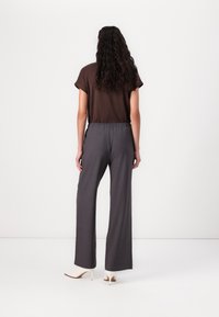 Haut marron à manches courtes associé à un pantalon gris taille haute à jambes larges. L'ensemble présente une coupe décontractée et une texture de tissu lisse.