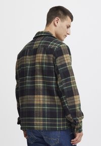 Ruitendons in zwart, groen en beige. Voorzien van een button-down kraag en lange mouwen, met een iets relaxte pasvorm.
