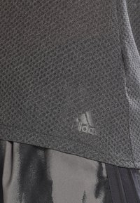 T-shirt sportif texturé gris foncé avec logo Adidas au-dessus d’un short noir et gris à motifs.