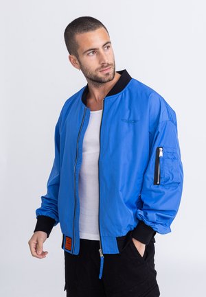 Blauwe bomberjack gemaakt van lichtgewicht stof, met een zwarte geribbelde kraag, een ritszak op de mouw en een contrasterend oranje label.