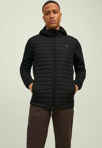 Schwarze, leichte Jacke mit gesteppter Vorderseite, Reißverschluss und Kapuze. Verfügt über seitliche Taschen und einen glatten, dehnbaren Stoff an den Ärmeln.