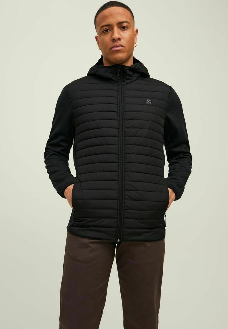 Schwarze, leichte Jacke mit gesteppter Vorderseite, Reißverschluss und Kapuze. Verfügt über seitliche Taschen und einen glatten, dehnbaren Stoff an den Ärmeln.