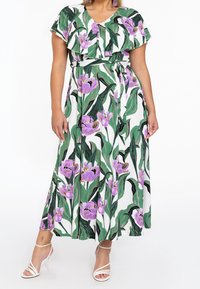 Maxiklänning med V-hals och volangärmar, prydd med ett blommönster i lila och grönt på en vit bakgrund. Knuten midjedetalj.