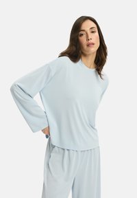 Jasnoniebieski top z długim rękawem z miękkiego materiału o luźnym kroju, okrągłym dekolcie i opadających ramionach, zestawiony z pasującymi spodniami.
