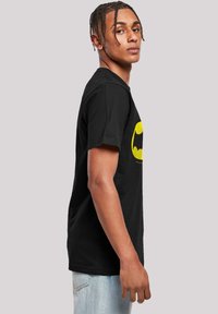 Sort bomulds t-shirt med gul Batman-logo, rund halsudskæring, korte ærmer og afslappet pasform. Bæres med lyseblå jeans.