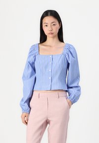 Blå og hvite.stripede kort blouse med pufferm, firkantet hals og knappestatus. Bæres med lyserøde skreddersydde bukser.