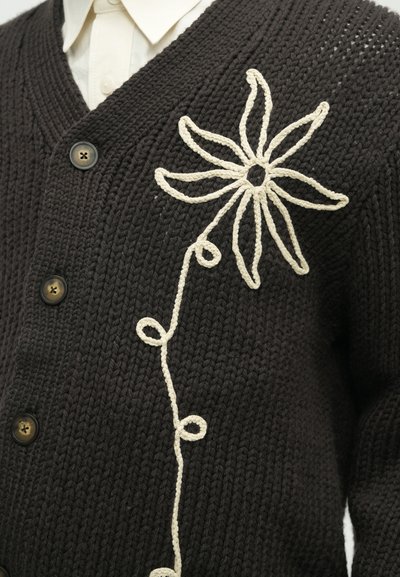 Sötétbarna, kötött kardigán, elülső részén egy nagy, krém színű virágmintával, kerek gombokkal és texturált kötött mintával.