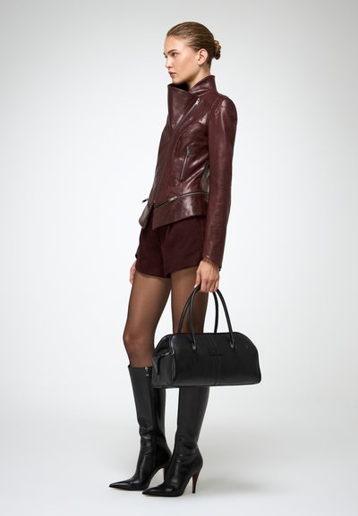 Burgundia nahkajope, millel on asümmeetriline tõmblukk, must kott, korralikult istuvad mustad põlvekõrgused saapad ja lühikesed burgundia šortsid.