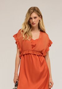 Vestido color óxido con un volante y mangas cortas, hecho de tela suave, con un escote en V profundo y una cintura ajustada.
