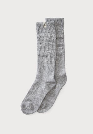 Par lange, lysegrå strikkede uldstrømper med ribbet kant og et lille beige UGG-mærke nær toppen.