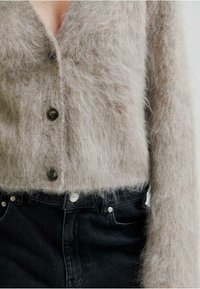 Ljusgrå, fluffig tröja med v-ringning, som har stora knappar och långa ärmar, kombinerad med höga svarta jeans.