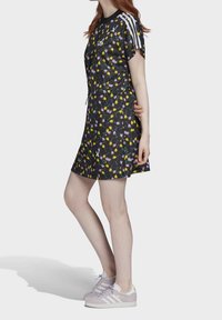 Černé šaty s krátkým rukávem, zdobené barevným květinovým vzorem, černým límečkem a bílými pruhy na ramenech; v kombinaci se světle fialovými teniskami.