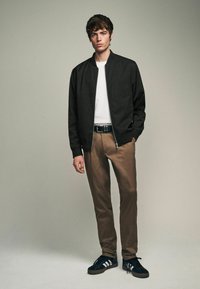 Crna bomber jakna preko bijele majice, kombinirana s smešnim hlačama i crnim tenisicama. Glatka tkanina i čiste linije kroz cijeli outfit.