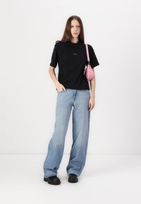 Black short-sleeve t-shirt with logo, light blue wide-leg jeans, and black chunky boots. A small pink handbag is slung over one shoulder.