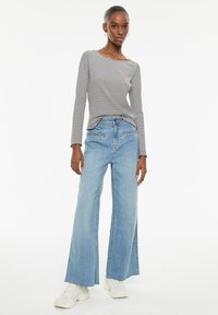 Zwart-wit gestreepte lange mouw top, gecombineerd met lichtblauwe wijde jeans. Witte sneakers maken de outfit compleet.