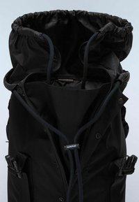 Mochila negra con cierre de cordón y correas ajustables. Presenta una textura de tela suave y una etiqueta de logo en el interior.