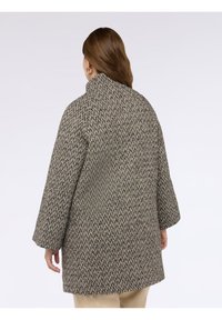 Cappotto a tartan marrone e beige con colletto alto, maniche ampie, tessuto testurizzato e vestibilità rilassata. Nessun hardware o accenti visibili.