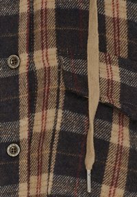 Skjorte i tern med en blanding af marineblå, beige og rød farve. Den har en blød tekstur, knaplukning og en hætte med snøre.