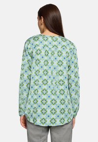 Koszula w kwiatowy wzór z długim rękawem w jasnoniebiesko-zielonych kolorach. Posiada okrągły dekolt oraz luźny krój z zaokrąglonym dołem.