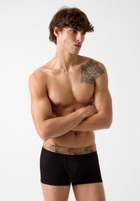 Boxer shorts neri con una vita a motivo camouflage e logo "GUESS" in rosso. Tessuto liscio, design aderente e taglio atletico.