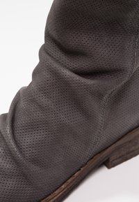 Botte de cheville en cuir gris avec texture perforée, design décontracté et talon en bois brun légèrement usé.