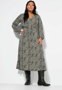 Schwarz-weißes Maxikleid mit floralem Muster, langen Ärmeln, V-Ausschnitt, tailliertem Bund und fließendem Rock, getragen mit schwarzenCowboystiefeln.