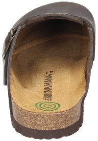 Braune Lederclogs mit Korksohle, offenem Zeh und verstellbarem Riemen. Das Innenfutter ist hellbeige mit einem Branding-Stempel und einem grünen Logodetail.