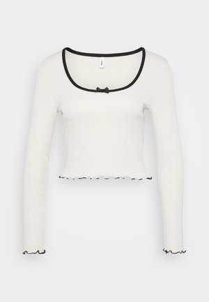 Valge pikki varrukatega lühike topp, millel on lai musta äärisega ümmargune kaelus, keskel kaarekuju detail ning volangiga must äär varrukatel ja allääres.