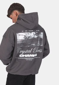 Felpa grigia con cappuccio caratterizzata da una grande grafica sul retro, raffigurante un'immagine in bianco e nero della Torre Eiffel, testo sulla parte superiore e una vestibilità rilassata.
