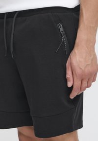 Svarta träningsshorts med elastisk midja, dragsko och dragkedjefickor på sidan. Tillverkade av ett mjukt tyg med en kroppsnära passform.