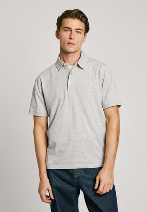 Polo gris de manga corta con cuello y tres botones. Diseño sencillo y textura suave. Llevado con jeans azul oscuro.