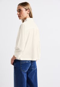 Vit, kortärmad skjorta med platt krage och knappdetaljer, parat med l�ösa, mörkblå denimjeans. Slät textur.