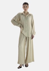 Ensemble beige en deux pièces avec une chemise boutonnée à manches longues et ample, accompagnée d'un pantalon à jambes larges orné d'un motif en chevron.