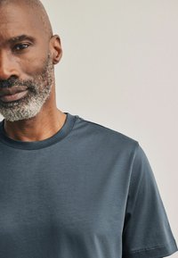 Camisa de manga corta color gris oscuro con cuello redondo, textura suave, brillo sutil y detalles de costura mínima a lo largo de la costura del hombro.