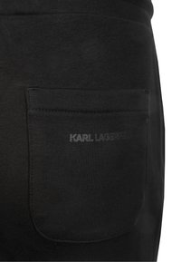 Schwarze Baumwoll-Jogginghose mit einer aufgesetzten Tasche und geprägt "KARL LAGERFELD"-Logo. Glatte Textur und körperbetontes Design.