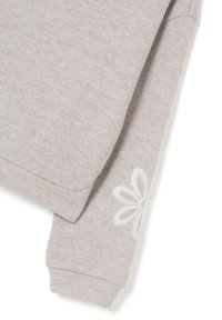 Felpa grigia chiara con una consistenza morbida, scollatura arrotondata e maniche lunghe con un dettaglio di ricamo floreale bianco sul polsino.