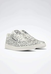 Baskets blanches avec des motifs complexes en lignes noires. Elles présentent un bout arrondi, un design à lacets et une marque Reebok sur le côté et la languette.