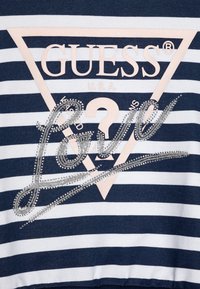 Sweatshirt rayé bleu marine et blanc avec un logo triangulaire portant le mot "GUESS" en rose clair et un "Love" argenté orné sur le devant.