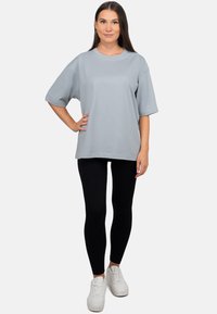 T-shirt oversize gris clair à manches courtes, en coton doux, associé à un legging noir et des baskets blanches.