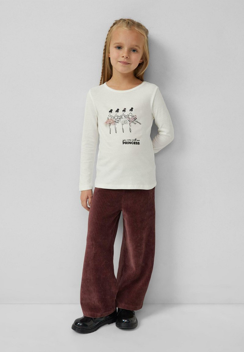 Langärmliges Creme-T-Shirt mit einer Ballerina-Grafik und dem Text "du kannst mich Prinzessin nennen", kombiniert mit weiten burgunderfarbenen Cordhosen und schwarzen Schuhen.
