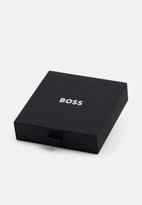Zwarte kartonnen doos met een gladde textuur, voorzien van een zilveren "BOSS" logo op de bovenkant en een uittrekbare handgreep voor opening.