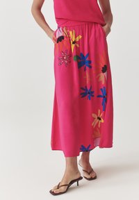 Jupe maxi florale rose avec une taille élastique, ornée de motifs de fleurs vives en jaune, bleu et rouge, avec des poches.