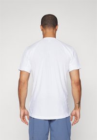 Bela športna majica s kratkimi rokavi, prilega se telesu in ima teksturirano hrbtno stran. Opremljena je z okroglo ovratnikom in subtilnimi linearnih vzorci za zračnost.