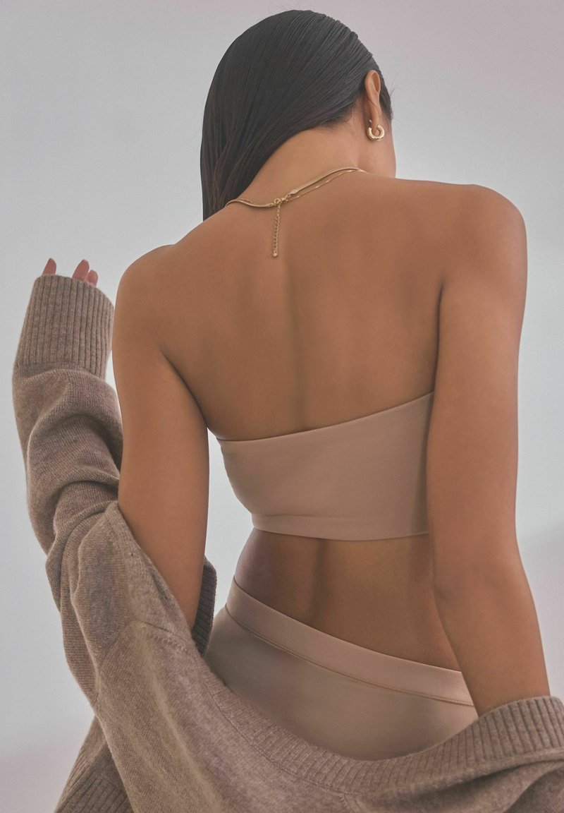 Beige cauruma tops un atbilstošas apakšbikses, kas apvienotas ar mīkstu, pārmērīgi lielu brūnu adījuma džemperi. Gluda auduma virsma ar subtilu spīdumu, minimāls aparatūras daudzums.
