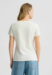 T-shirt crème à manches courtes avec un col rond, fabriqué en tissu de coton doux, présentant une coupe décontractée et une texture lisse.