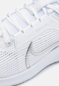 Primer plano de la zapatilla de correr Nike Pegasus 40 en blanco, mostrando la parte superior de malla, los cordones y el logo reflectante de Nike en el costado.