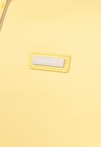 Superficie gialla texture con una toppa rettangolare argentata con il logo "HEXAGONA", contornato da cuciture gialle coordinate.