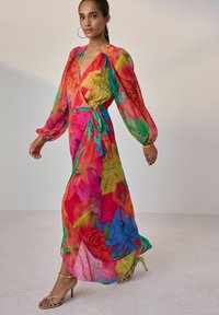 Rochie maxi dintr-o țesătură translucidă, colorată, cu imprimeuri florale mari în nuanțe de roz, verde și albastru. Mâneci lungi cu manșete elastice și talie legată.